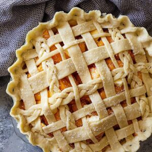Top down view of a peach pie with an all butter crust lattice top.