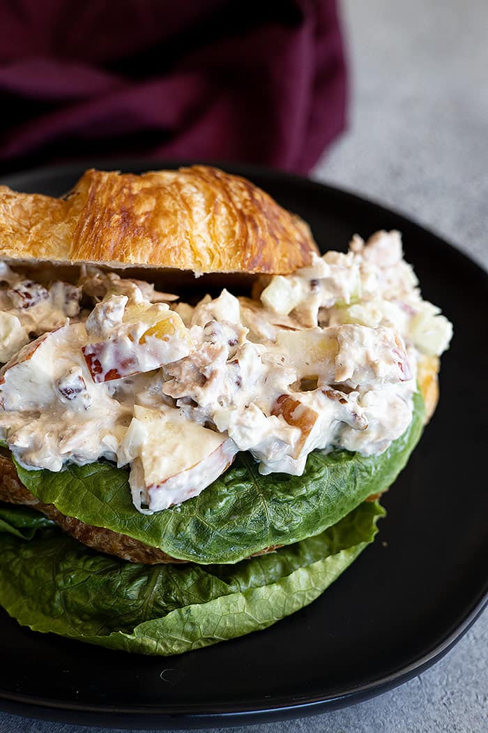 Apple tuna salad piled on a buttery croissant with a leaf of lettuce.. 