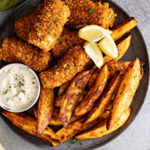 Overhead view of fish and chips on a plate garnished with lemon wedges. Tartar sauce off to the side.