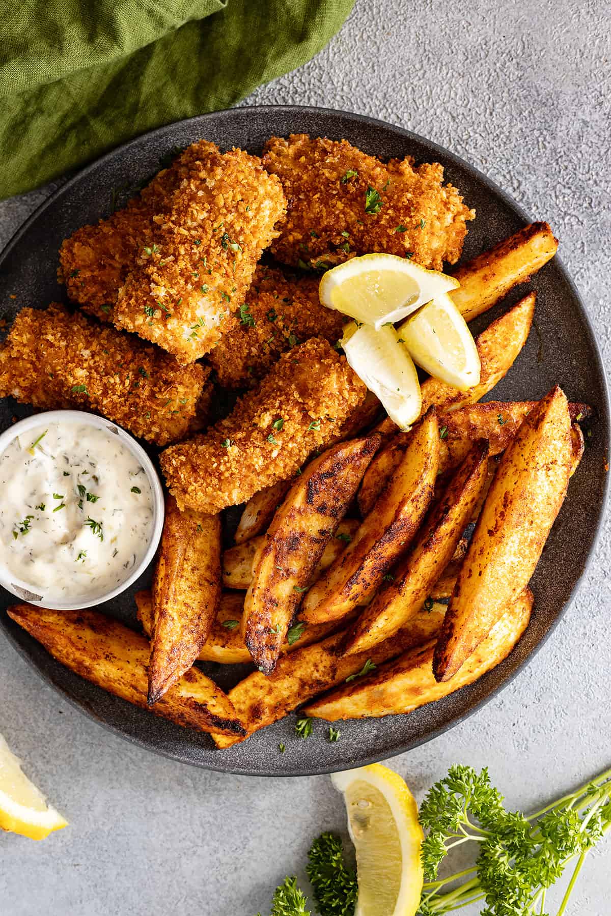 Overhead view of fish and chips on a plate garnished with lemon wedges. Tartar sauce off to the side.