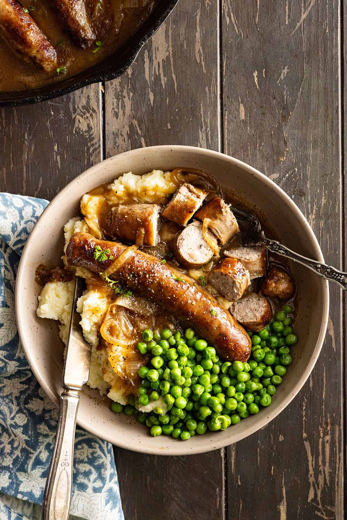 Overhead view of bangers and mash cut up on a plate with fork and knife on the plate ready to dive in.