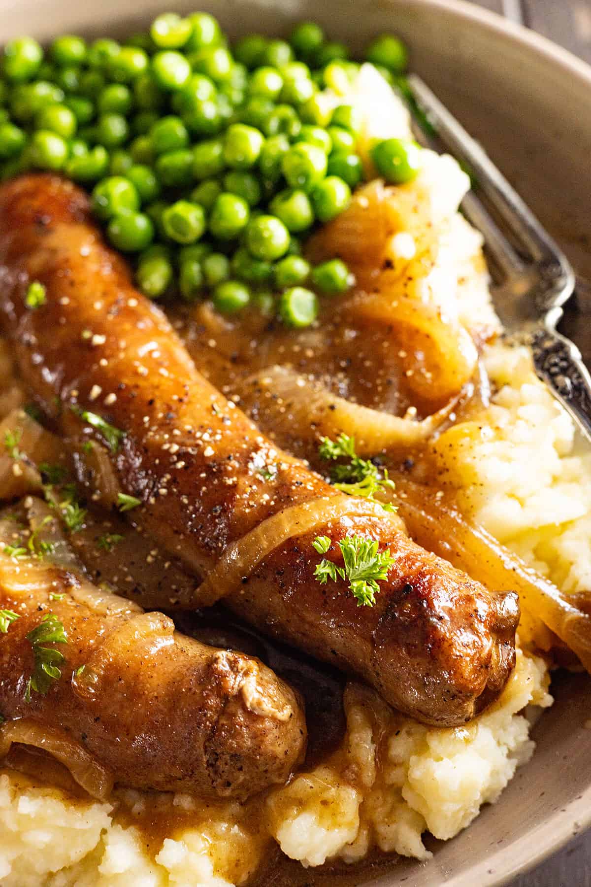 Close up of bangers and mash on a plate with peas. 