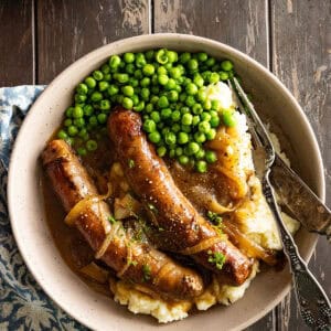 Overhead picture of bangers and mash on a plate with peas on the side.