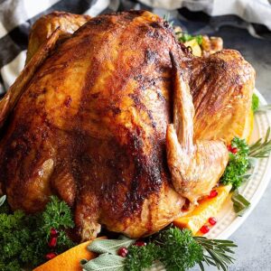 Beer and Butter Turkey on a platter decorated with fresh herbs, sliced oranges, and pomegranate seeds.