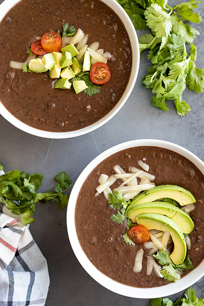 Two bowls of soup garnished with cheese, avocado, and cilantro. Bunches of cilantro in the corner of the picture.