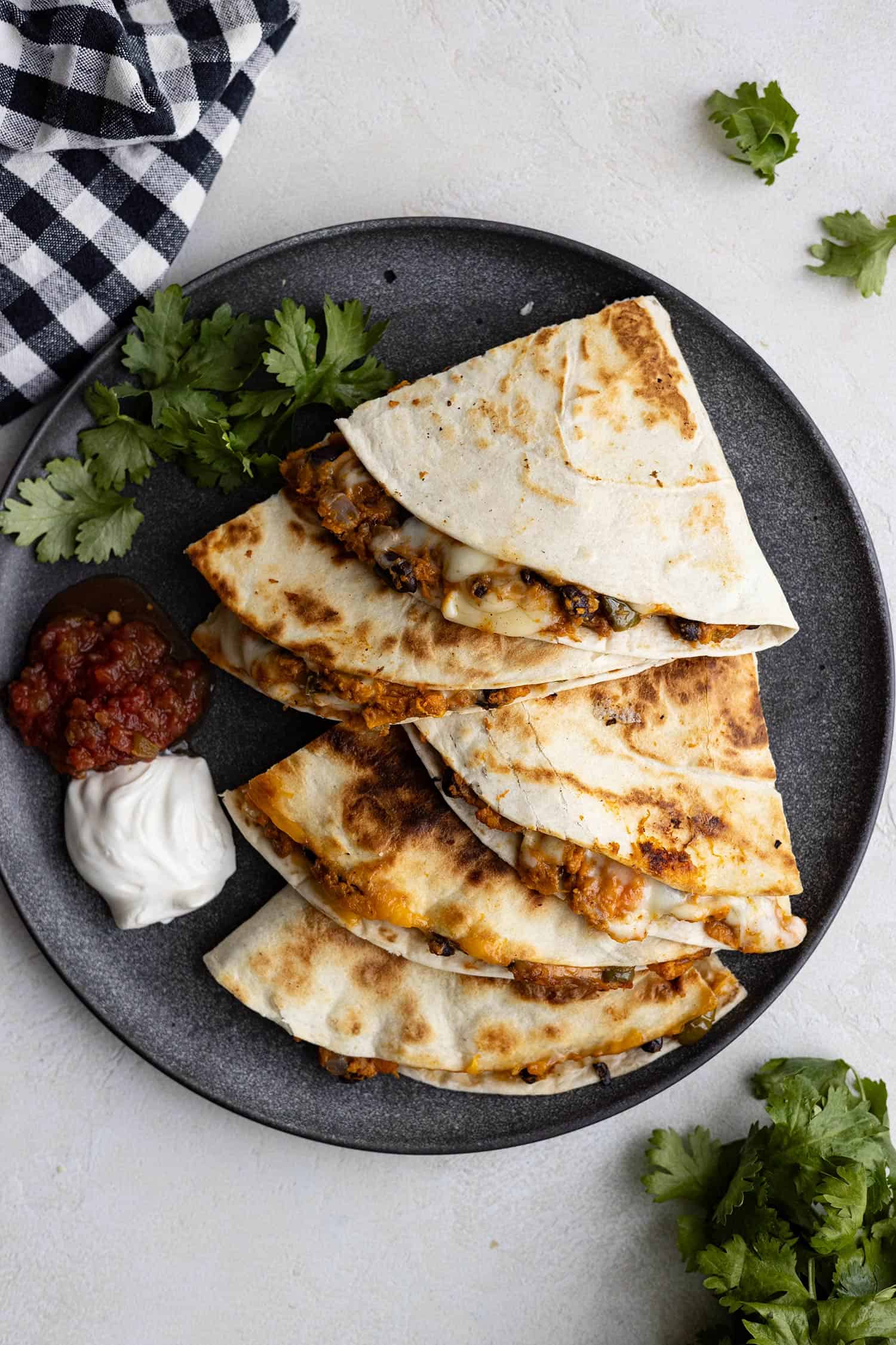 Overhead view of quesadillas on a dark plate with sour cream and salsa off to the side. 