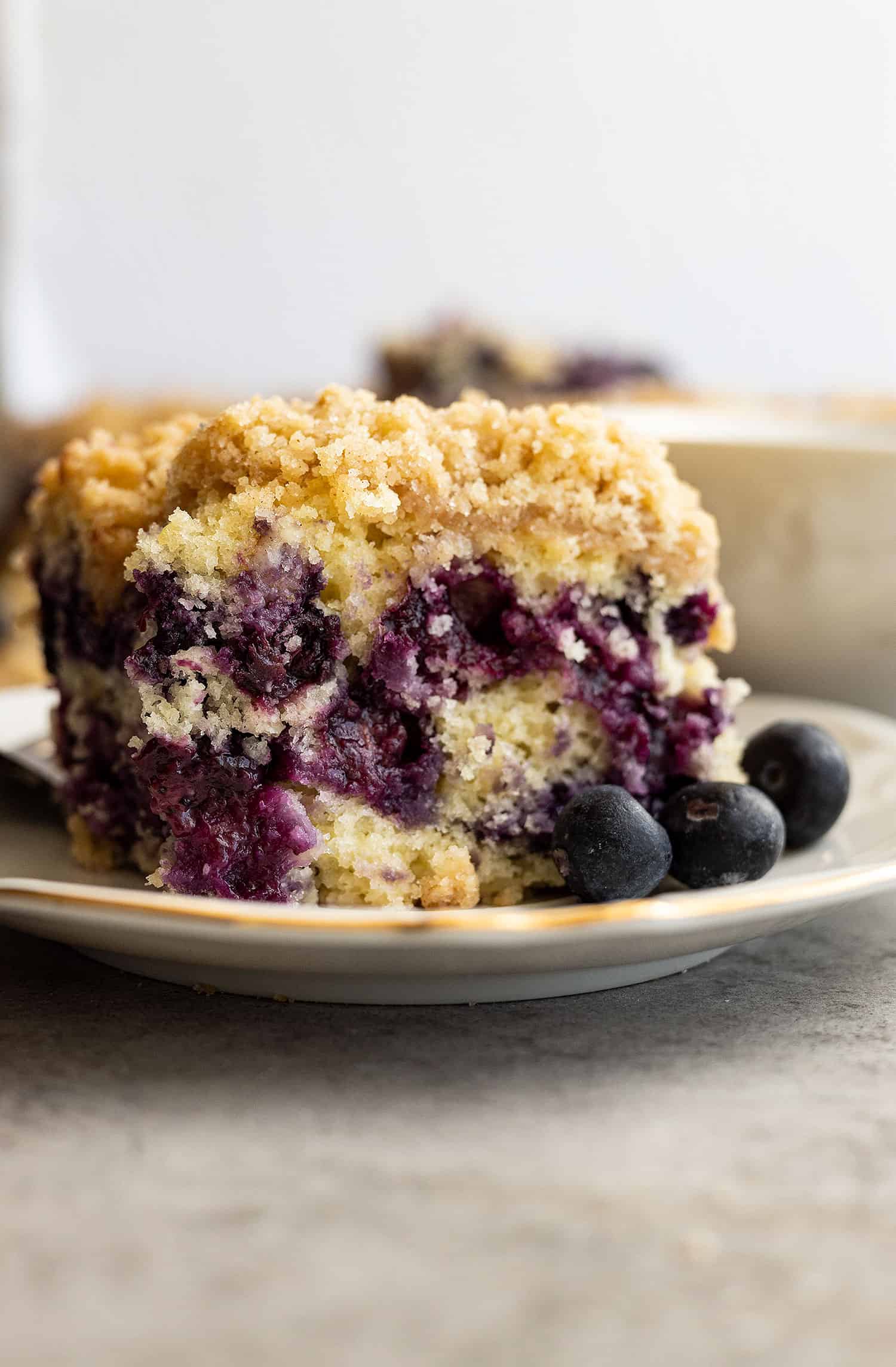 Blueberry buckle on a plate with blueberries off to the side. 