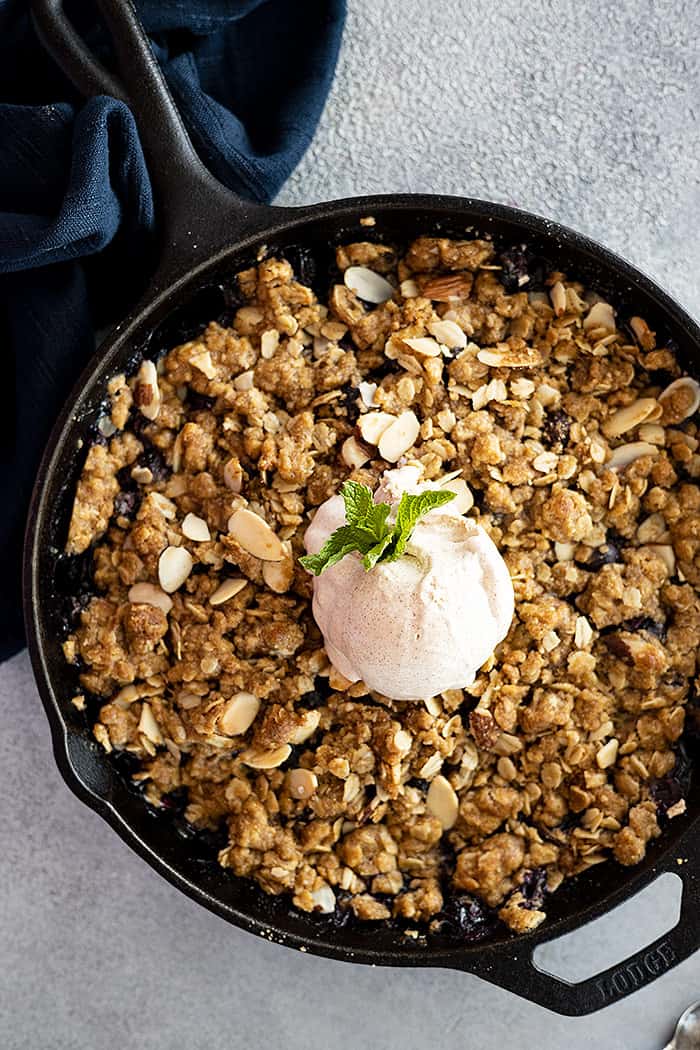Overhead view of blueberry crisp fresh from the oven. Topped with a big scoop of ice cream and a piece of fresh mint.