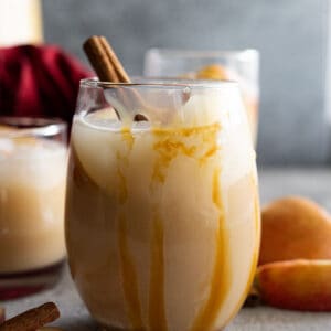 Sangria in a glass with caramel drizzle down the side. Apple slices and cinnamon stick to garnish.