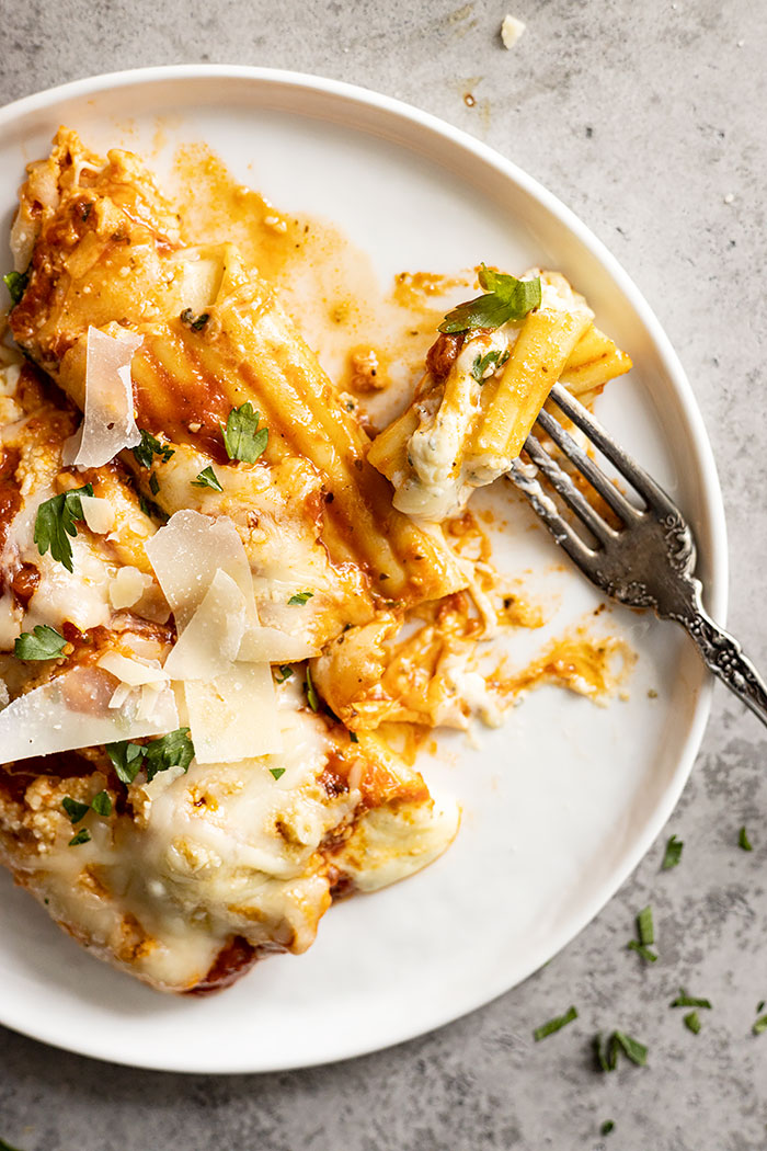Overhead view of a fork taking a bite sized piece of manicotti. 