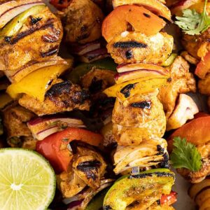 Close up picture of grilled chicken kebabs. Garnished with lime slices and cilantro.