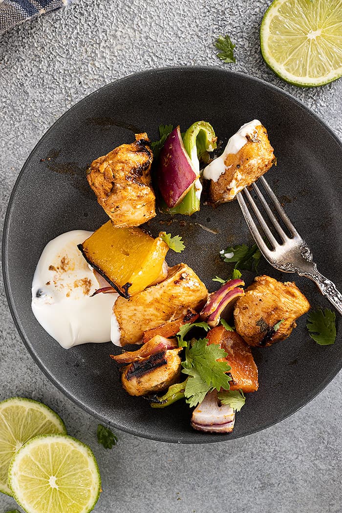 Pieces of kebab removed from the skewer and served on a plate with sour cream and garnished with cilantro. 