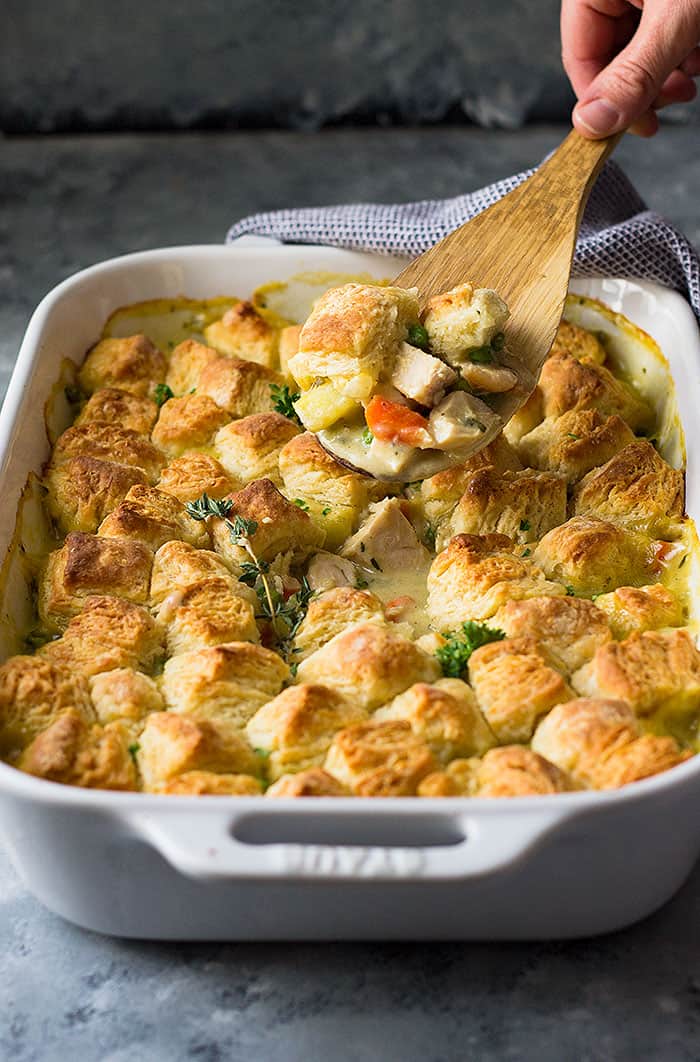 Wooden spoon scooping out chicken pot pie from white baking dish. 