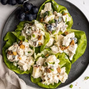Overhead picture of salad in lettuce leaves on a plate. A bunch of grapes in the corner and a light colored napkin to the side.