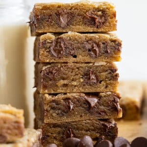 Tall stack of chocolate chip cookie bars next to a tall glass of milk.