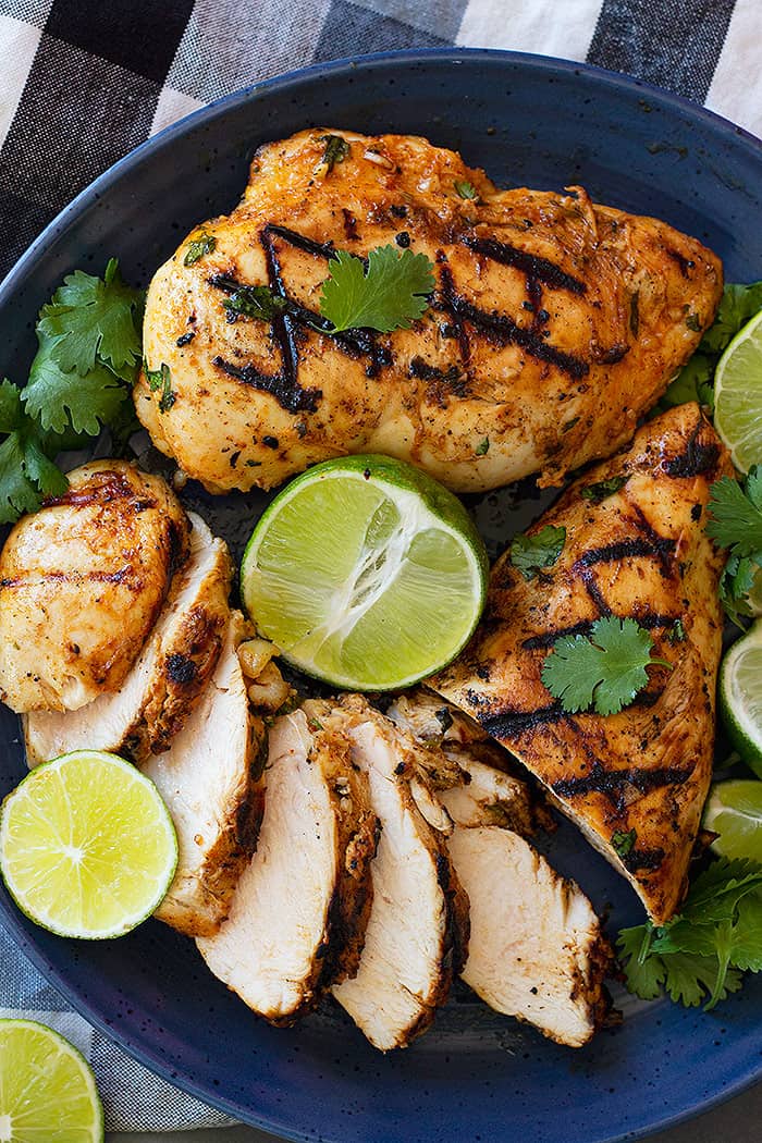 Sliced chicken on a blue plate garnished with cilantro and limes. 