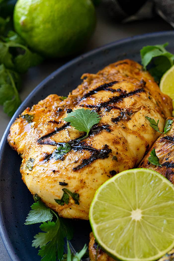 Grilled chicken on a blue plate garnished with lime and cilantro. 