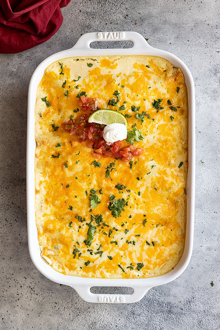 Overhead view of enchiladas from the oven garnished with lime, sour cream, and pico de gallo.