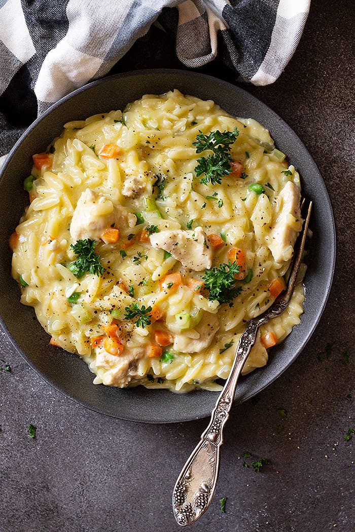 Top down image of orzo being served in a dark blue bowl and garnished with black pepper and parsley. 