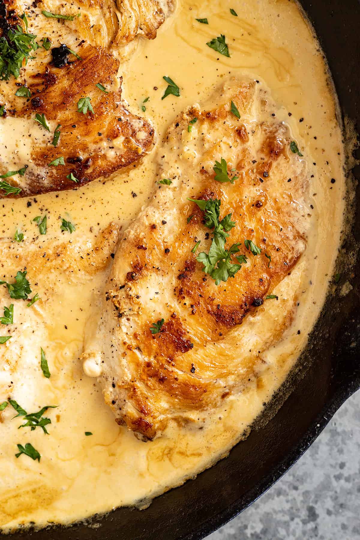 Close up of chicken in a cast iron pan. Garnished with fresh parsley. 