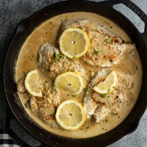 Overhead view of creamy lemon chicken in a cast iron skillet garnished with lemon slices and parsley.