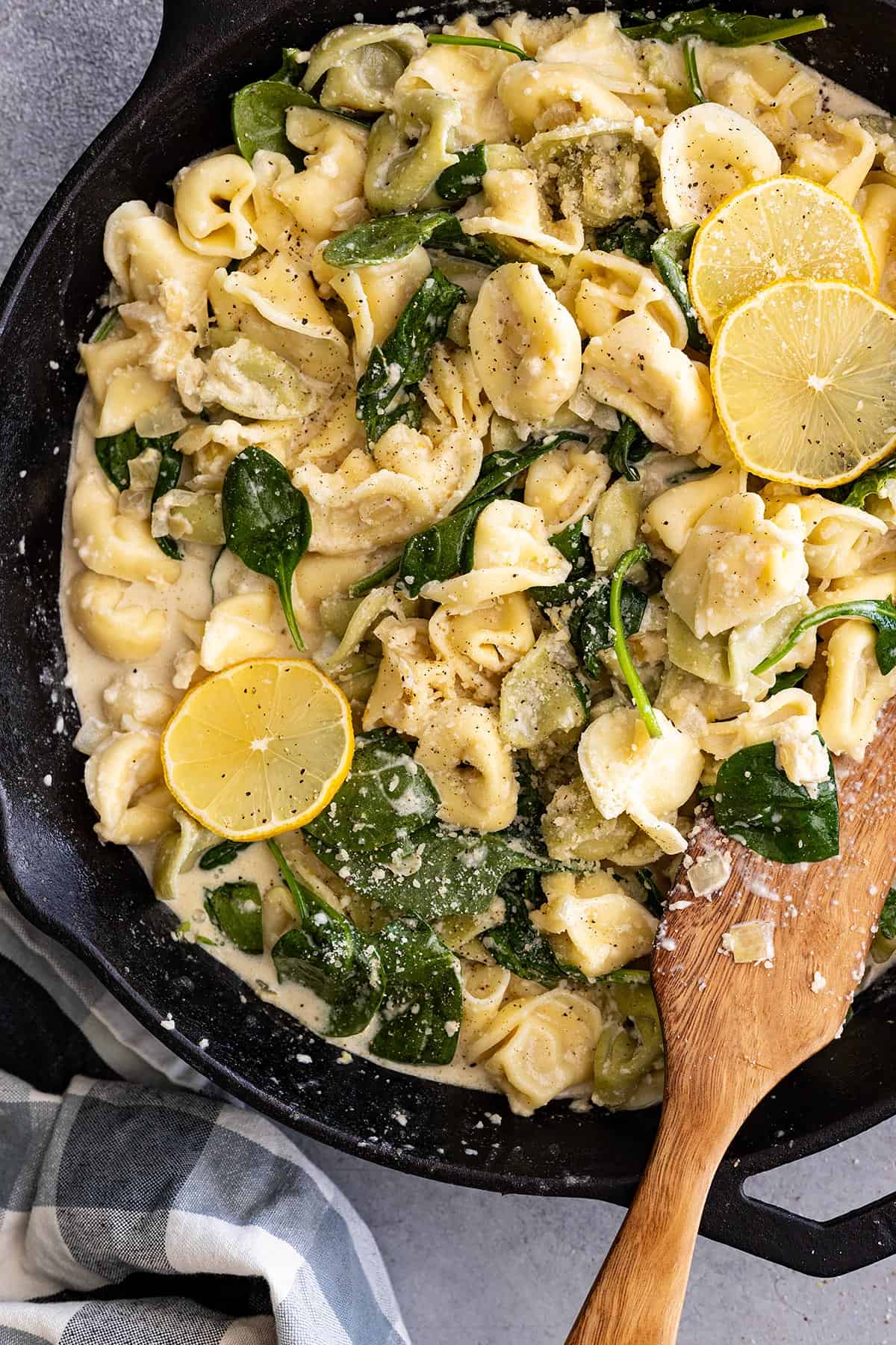 Overhead view of creamy lemon tortellini in a skillet with wood spatula to the side. 