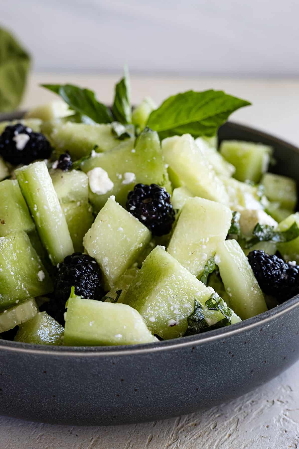 Side view of salad in a blue bowl with a sprig of basil for garnish. 