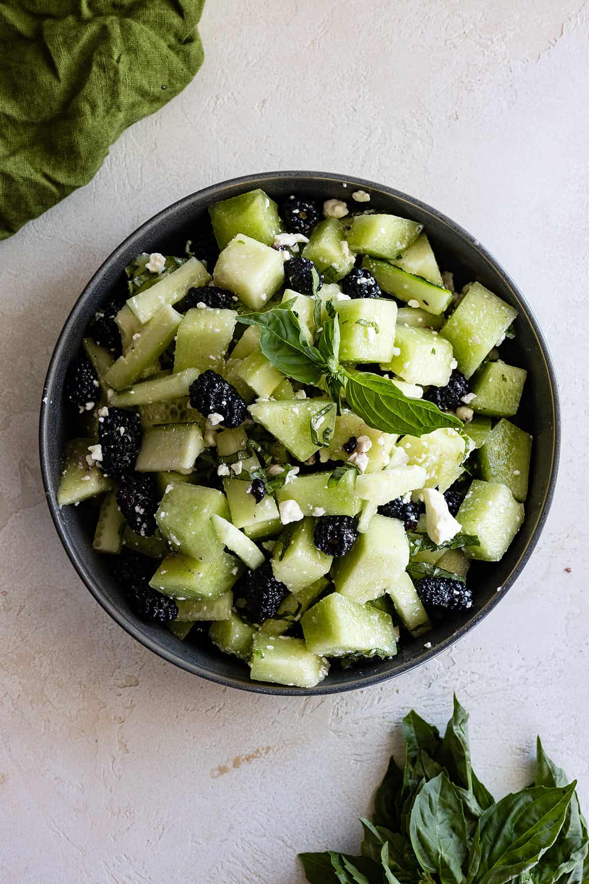 Overhead view of cucumber honeydew salad in a bowl with basil off to the side. 