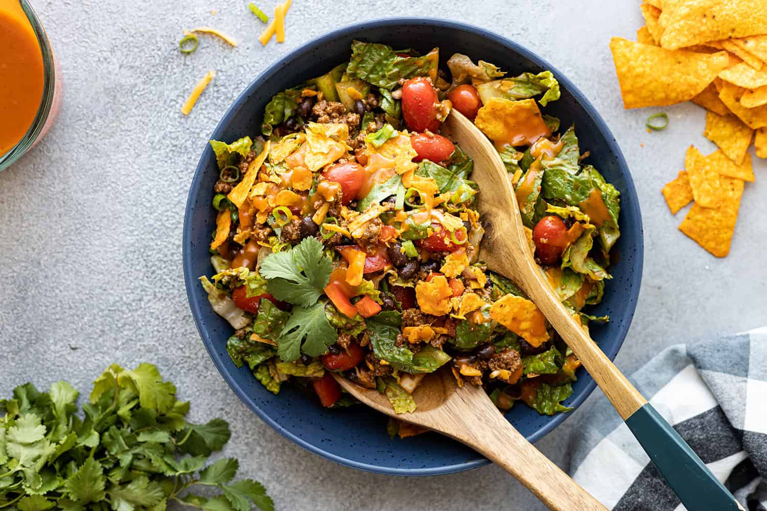 Overhead view of dorito taco salad in a blue bowl with serving utensils getting ready to serve the salad. 