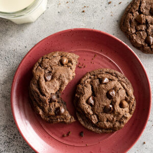 Cookies on a red plate with visible crumbs around and a glass of ice cold milk.