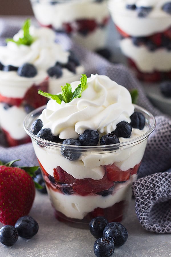 Plastic cup layered with cheesecake filling, berries, and whipped cream.