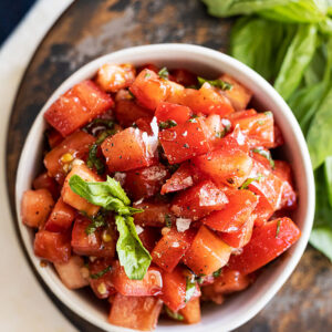 Overhead view of bruschetta in a bowl garnished with a basil leaf and flakey sea salt.