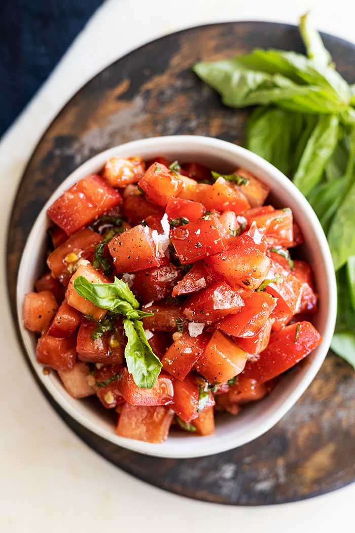 Overhead view of bruschetta in a bowl garnished with a basil leaf and flakey sea salt. 