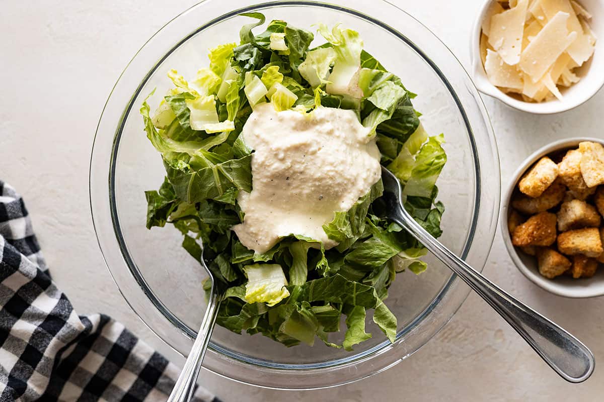 Overhead of salad being tossed in a bowl. Garnishes off to the side. 