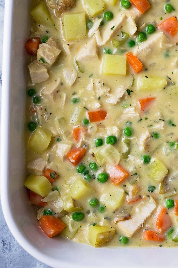 Chicken pot pie filling inside of white baking dish before adding biscuits. 