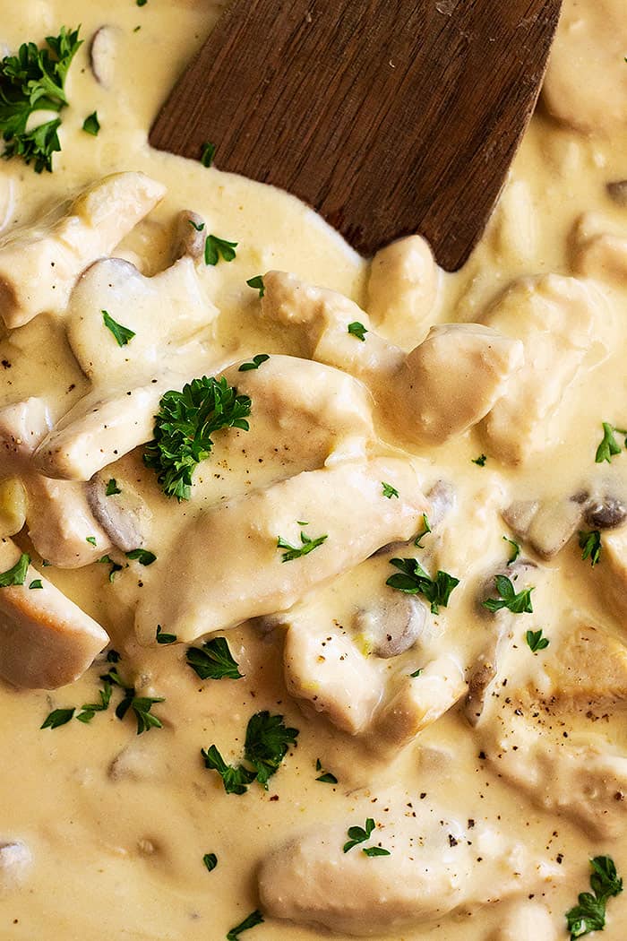 A close up of chicken stroganoff garnished with chopped parsley and black pepper. 
