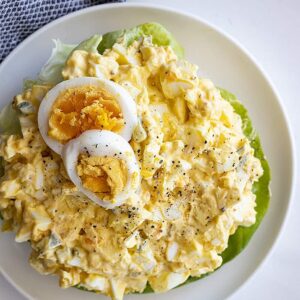 Overhead view of a large bowl of egg salad. Topped with 2 slices of hard boiled egg and fresh ground pepper.