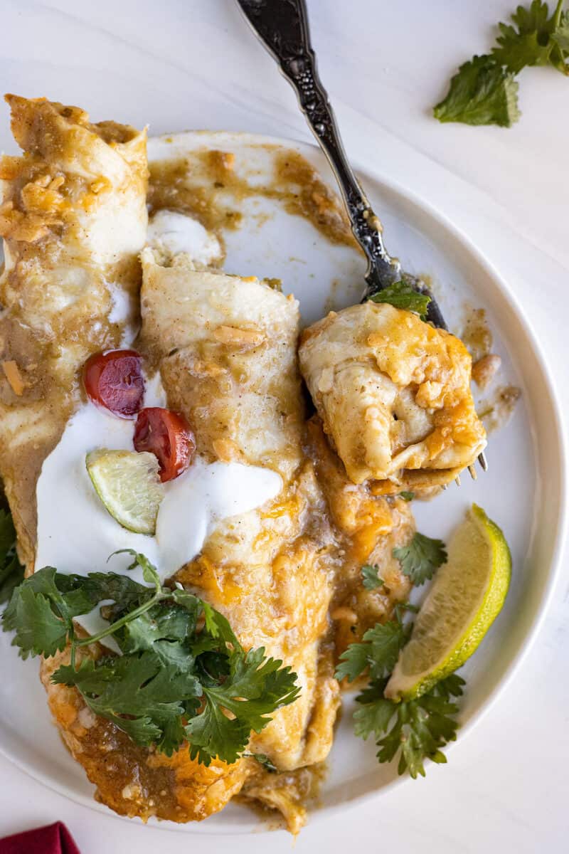 Overhead view of enchiladas on a plate with a fork taking a bite out. 