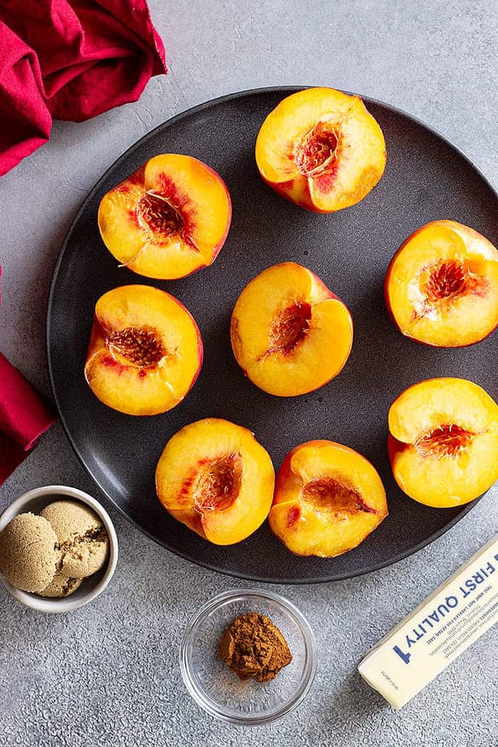 Top down grilling peaches ingredients. Peaches sliced in half, brown sugar, butter, and cinnamon are visible.