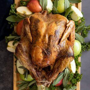 Overhead view of Herb Roasted Turkey on a cutting board garnished with apples and herbs.