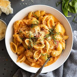 Overhead view of pasta with sauce in a white bowl. Garnished with fresh basil and parmesan cheese.