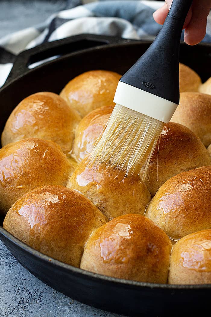 Melted butter being brushed on freshly baked dinner rolls.
