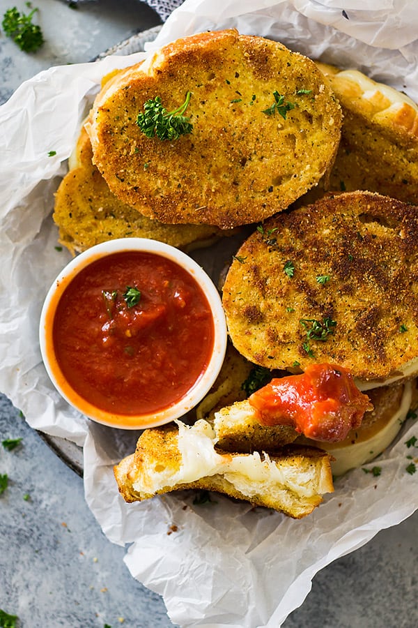 Top shot of Italian grilled cheese sandwiches next to small while bowl of pizza sauce.