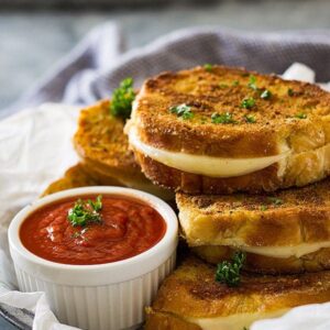 Grilled cheese sandwiches next to small while bowl of pizza sauce.