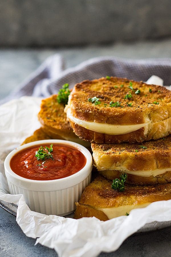 Grilled cheese sandwiches next to small while bowl of pizza sauce.