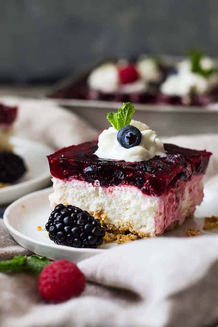 side view: a slice of Jello pretzel dessert topped with whipped cream and berries with 3 layers showing