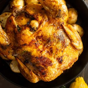 Overhead view of roasted chicken fresh from the oven. Lemon and fresh herbs off to the side.