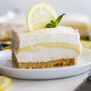 A piece of lemon dessert on a plate garnished with a lemon slice and mint.