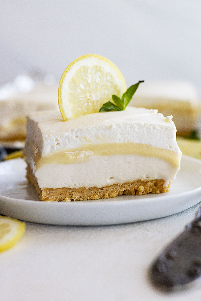 A piece of lemon dessert on a plate garnished with a lemon slice and mint. 