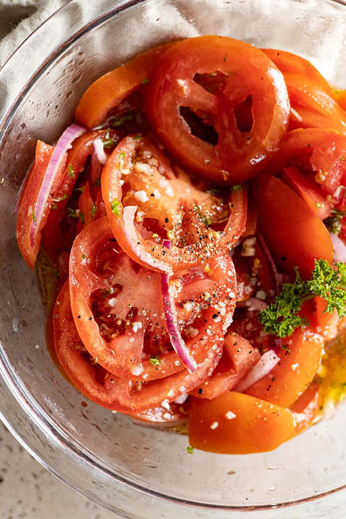 extreme closeup: my marinated tomato recipe in a bowl garnished with cracked pepper and flaky salt
